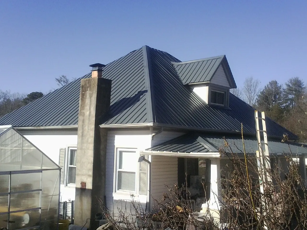 Dark blue standing seam metal roof on a white farmhouse with dormer — Slate & Tile Roof Repair by Roofing Brothers in Caddo Mills