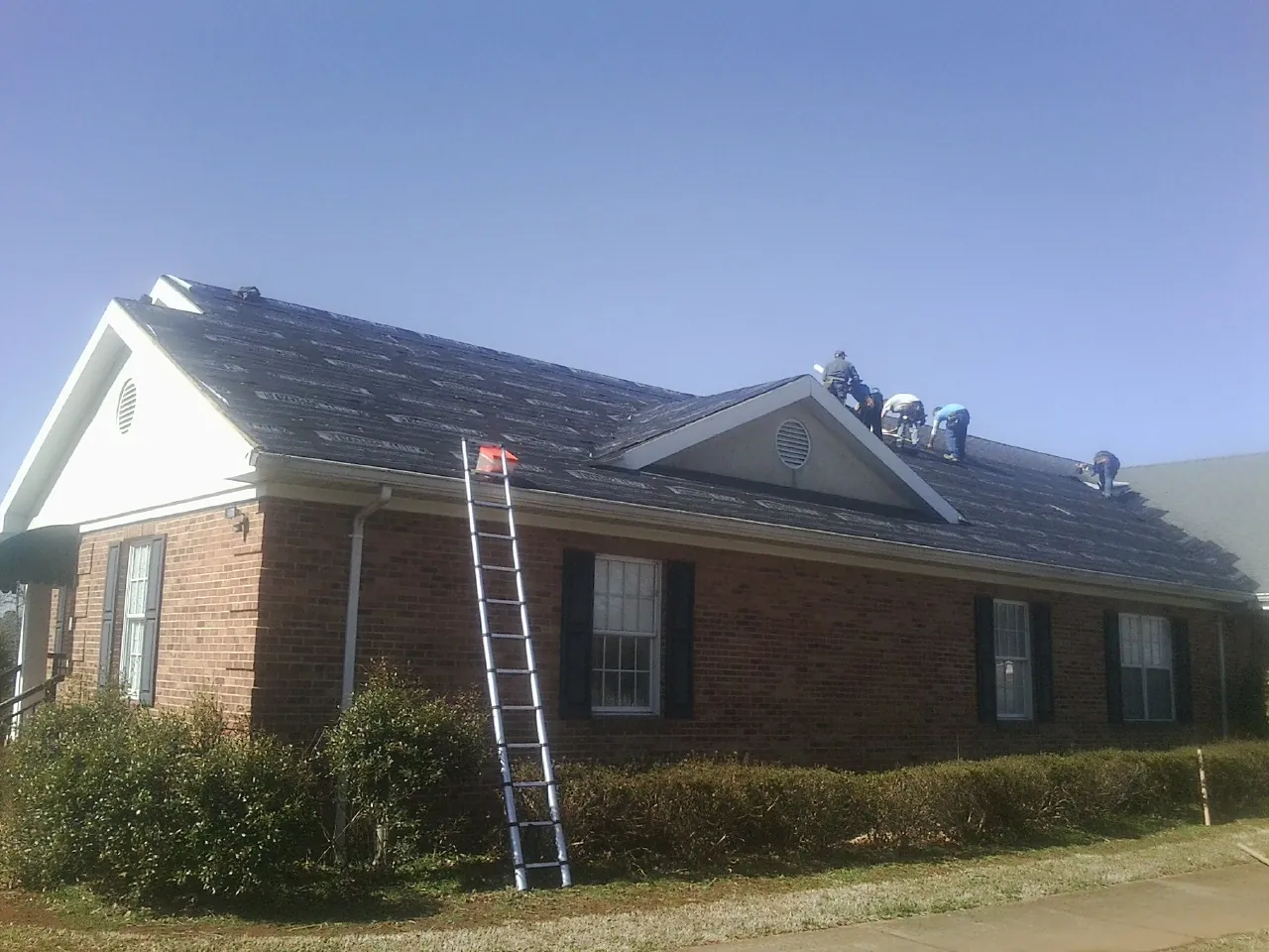 Crew tearing shingles off a brick ranch roof with a ladder set — Metal Roof Repair work by our crew in Caddo Mills