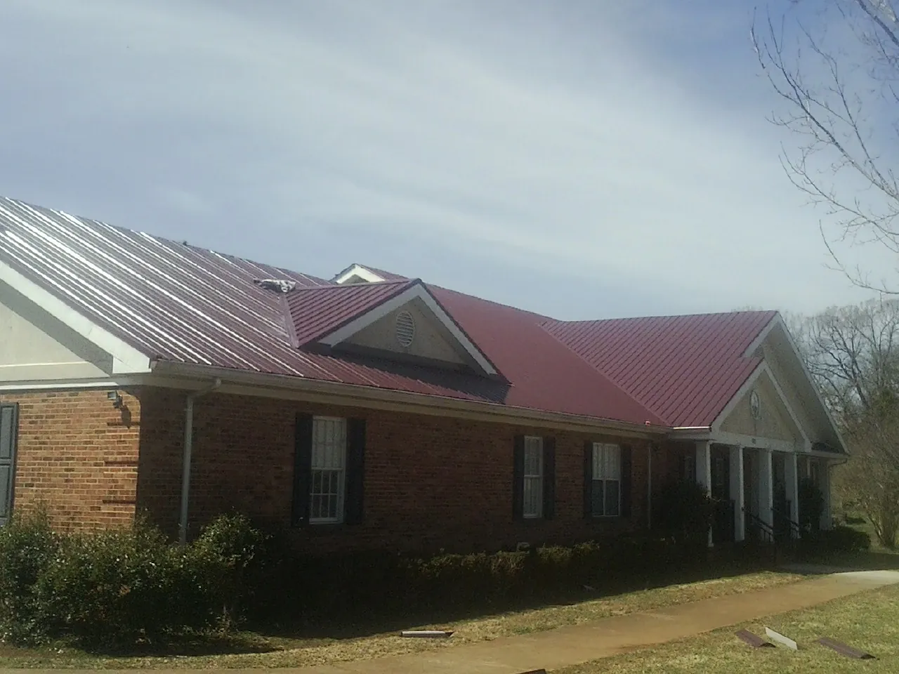 Red metal roof with gabled entries on a long brick building, from a Hail Damage Roof Repair job in Caddo Mills