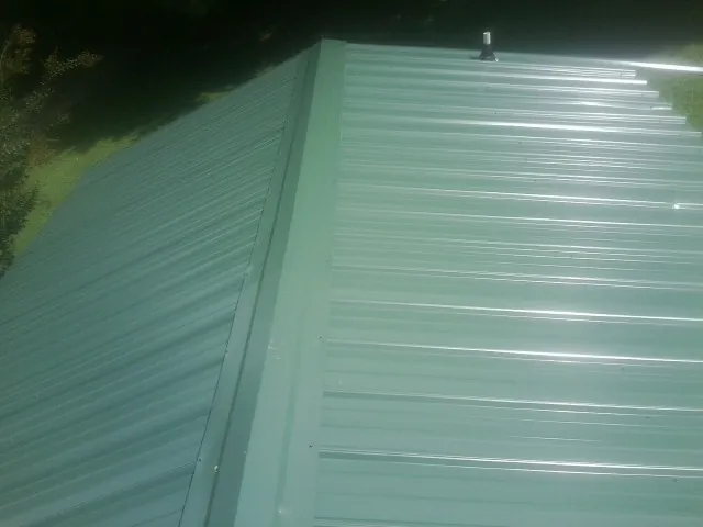 New green metal panels meeting at the ridge of a roof — Flat Roof Repair work by our crew in Caddo Mills