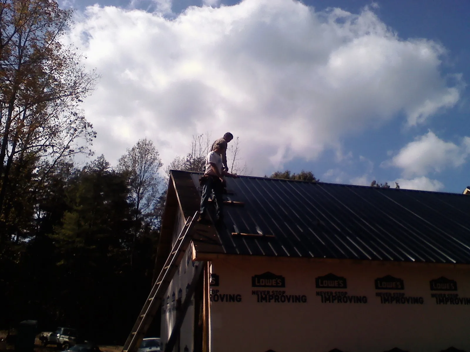 Roofer fastening dark metal panels high against a cloudy sky, from a Roof Inspection job in Caddo Mills