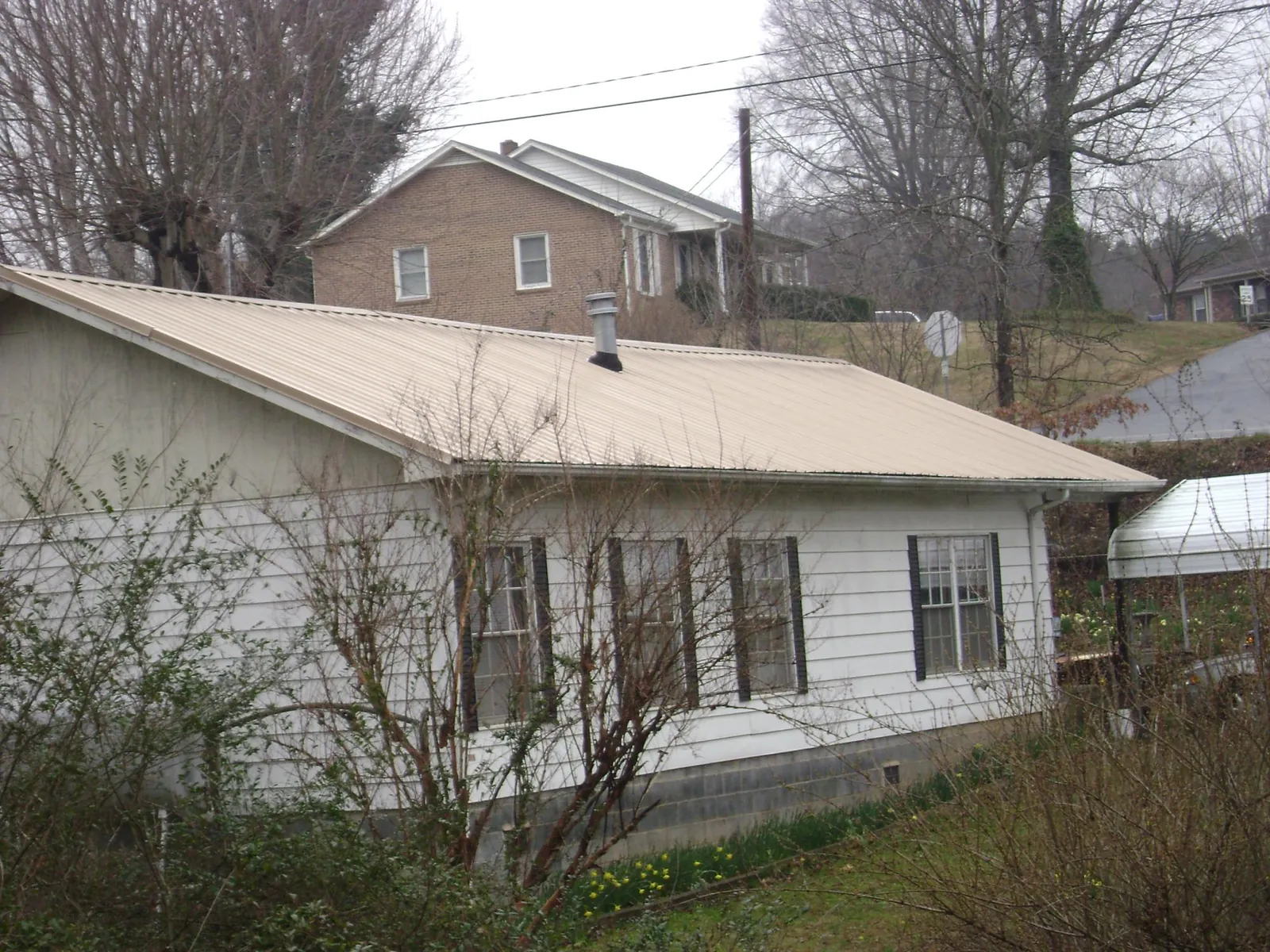 Tan metal roof on a white sided house set into a hillside — Commercial Roofing by Roofing Brothers in Caddo Mills