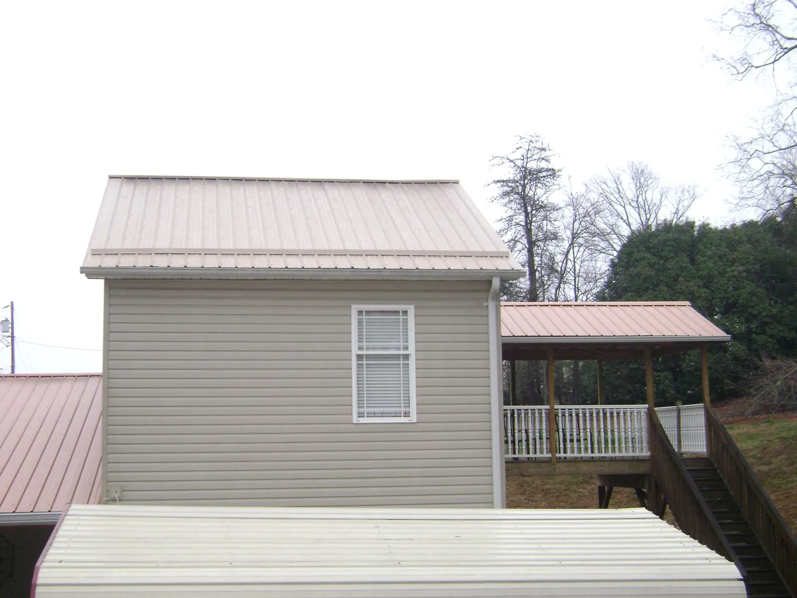 Tan metal roofs on a two story addition and attached porch, from a Roof Replacement job in Caddo Mills